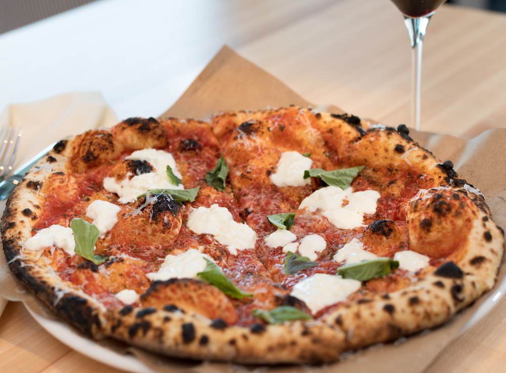 This photo shows a beautiful Margherita pizza with a glass of wine.