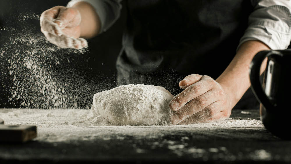 Male chef hands knead dough with flour on kitchen table side view