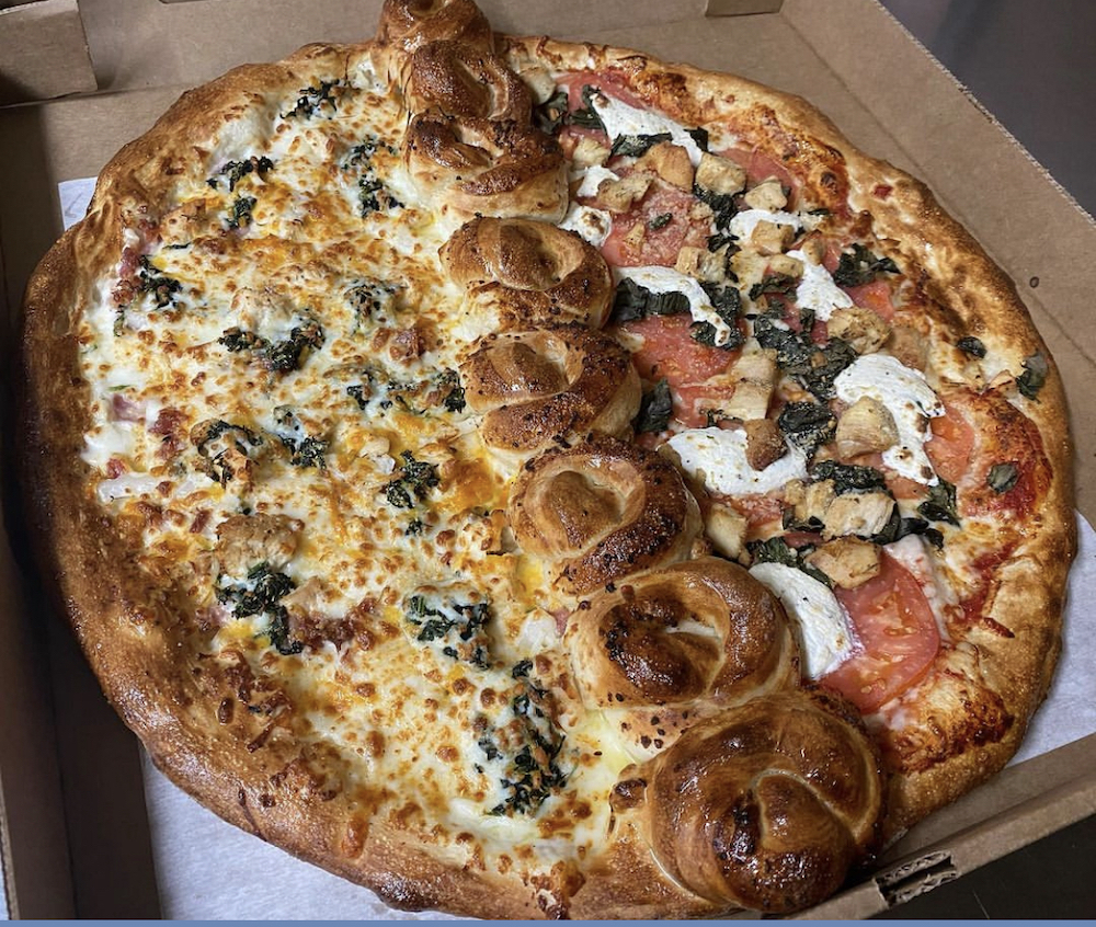 This photo shows a delicious-looking pizza with a row of garlic knots baked into the middle, splitting the pizza into two, each with different toppings.