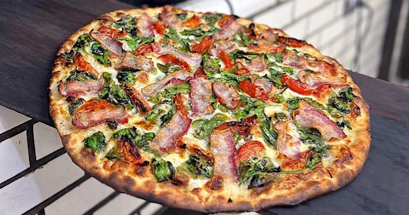 This photo shows Frank Pepe's Spring Special pizza, featuring mozzarella, roasted tomatoes, spinach, bacon, Pecorino Romano cheese and a drizzle of olive oil. 