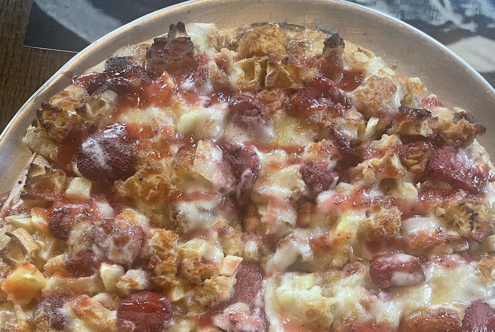 A pizza featuring spiced cinnamon cream cheese base topped with breaded chicken tenders, chunks of buttermilk waffles, strawberries, pineapple, cinnamon, sugar and mozzarella cheese. The pie is topped with a strawberry and pineapple puree glaze.