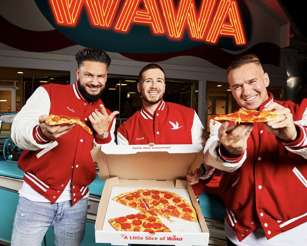 Three men stand with an open Wawa Pizza box, ready to eat pizza.