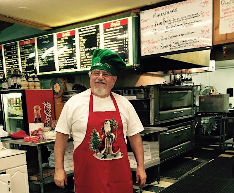 this photo shows Elvio Decilla in a red Christmas-themed apron and a green hat in his restaurant.