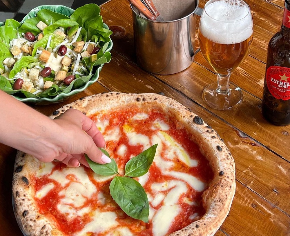 This photo shows a woman's hand adding basil leaves to a Margherita pizza.