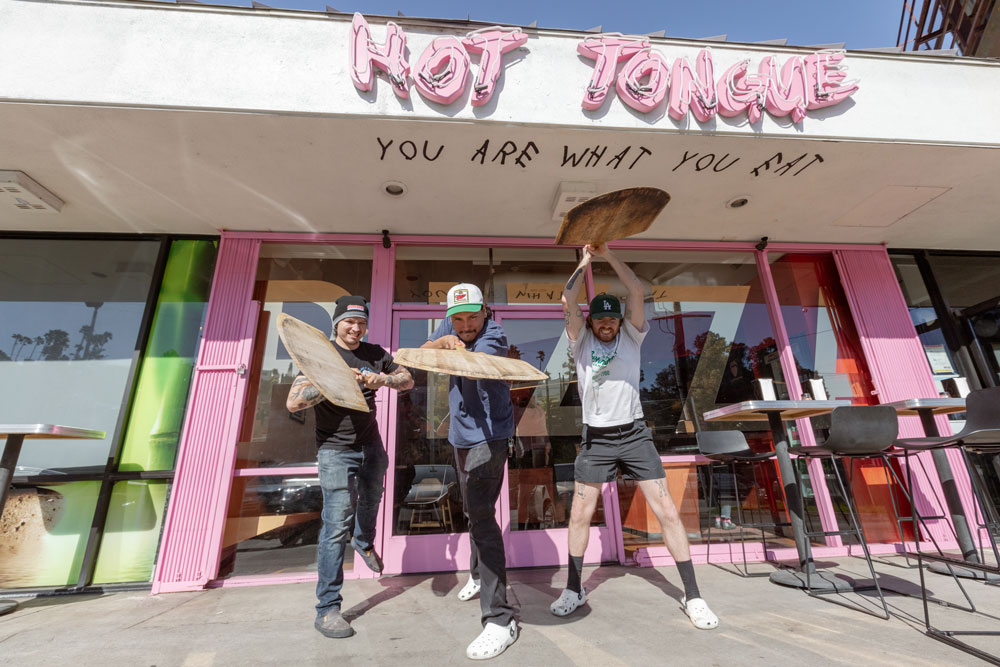 This photo shows three Hot Tongue Pizza employees wielding their pizza peels in comedic fashion in front of the restaurant.