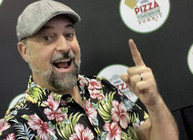 This shows a man with a graying beard and a Hawaiian shirt pointing at a floating circle with the words Pizza Tomorrow Summit