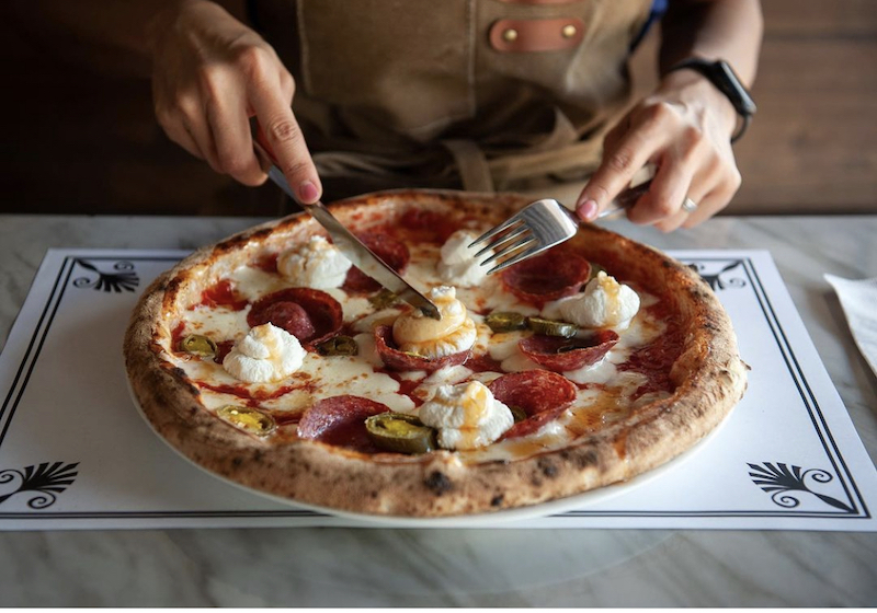 This photo shows someone getting ready to cut into a whole pizza topped with swirls of ricotta, pepperoni and jalapeños 