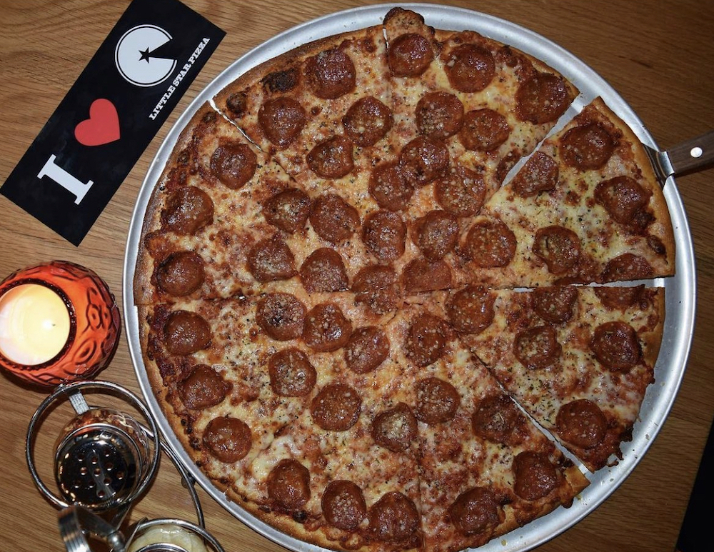 This photo shows a large pepperoni pizza with a couple of glasses of wine and a little candle.