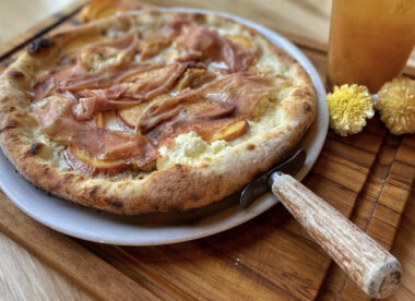 This photo shows a pizza topped with peaches and prosciutto from Maialina.