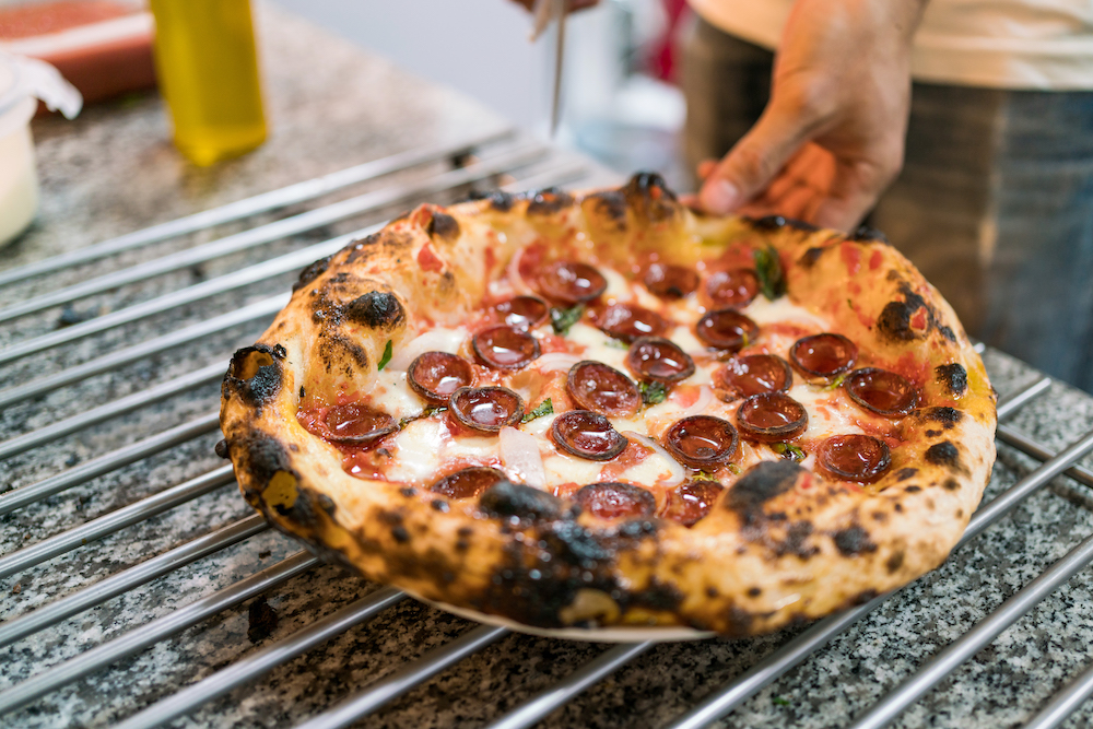 This photo shows a hand removing a slice of a Neapolitan pizza with a beautifully blistered crust.