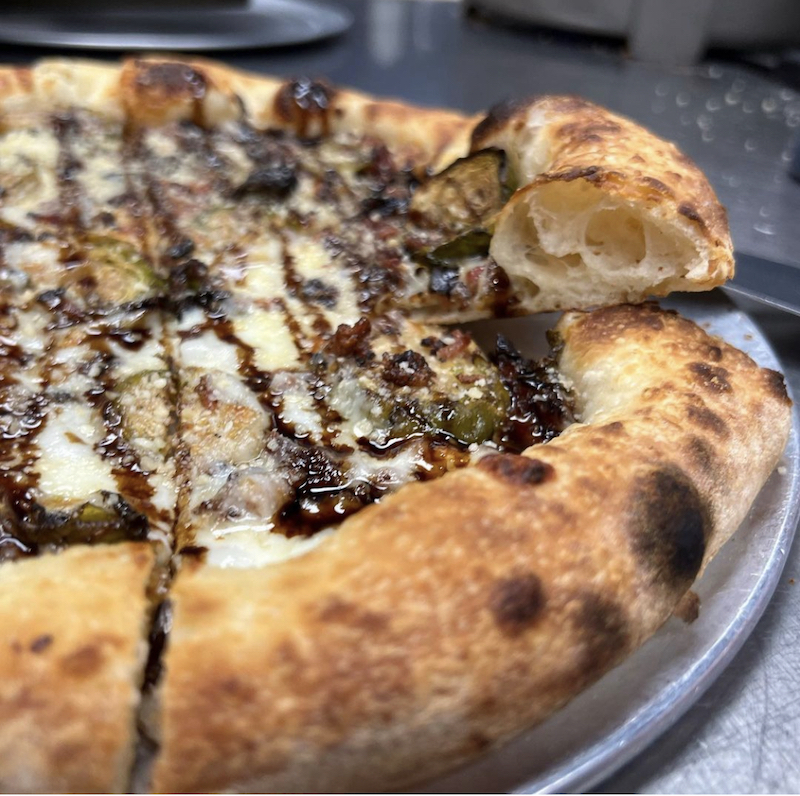 This photo shows a pizza topped with mozzarella, roasted Brussels sprouts, balsamic glaze and grated Parmesan.