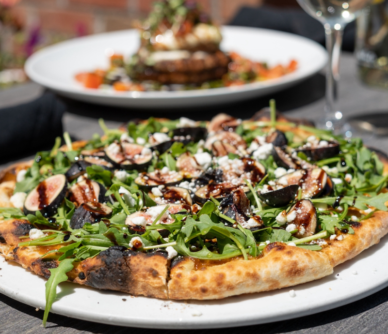 This photo shows a beautiful pizza topped with figs, arugula and goat cheese.