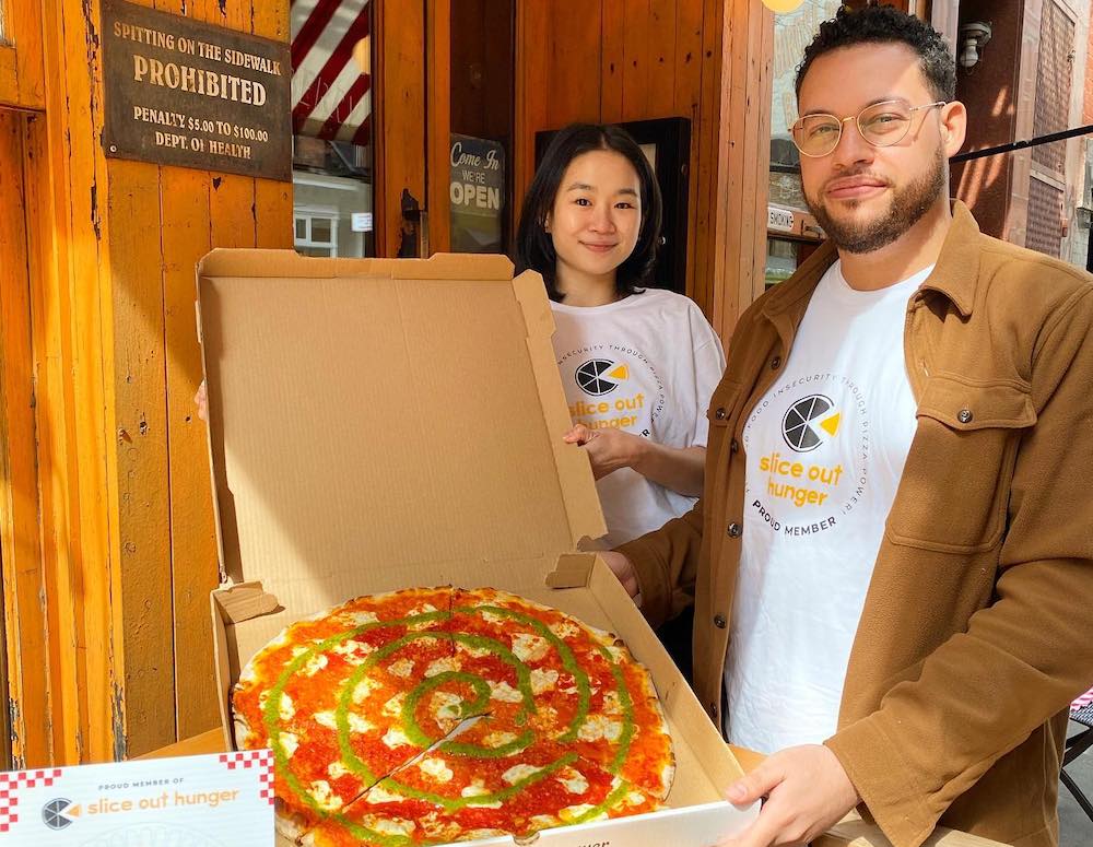 This photo shows a man and a woman standing in front of Rubirosa's entrance with a pizza in a carryout box.