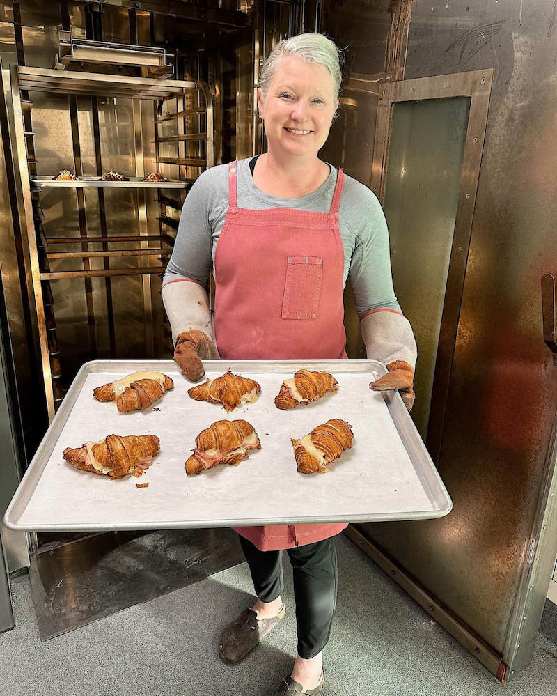 This photo shows Chef Kerri holding a tray with six croissants.