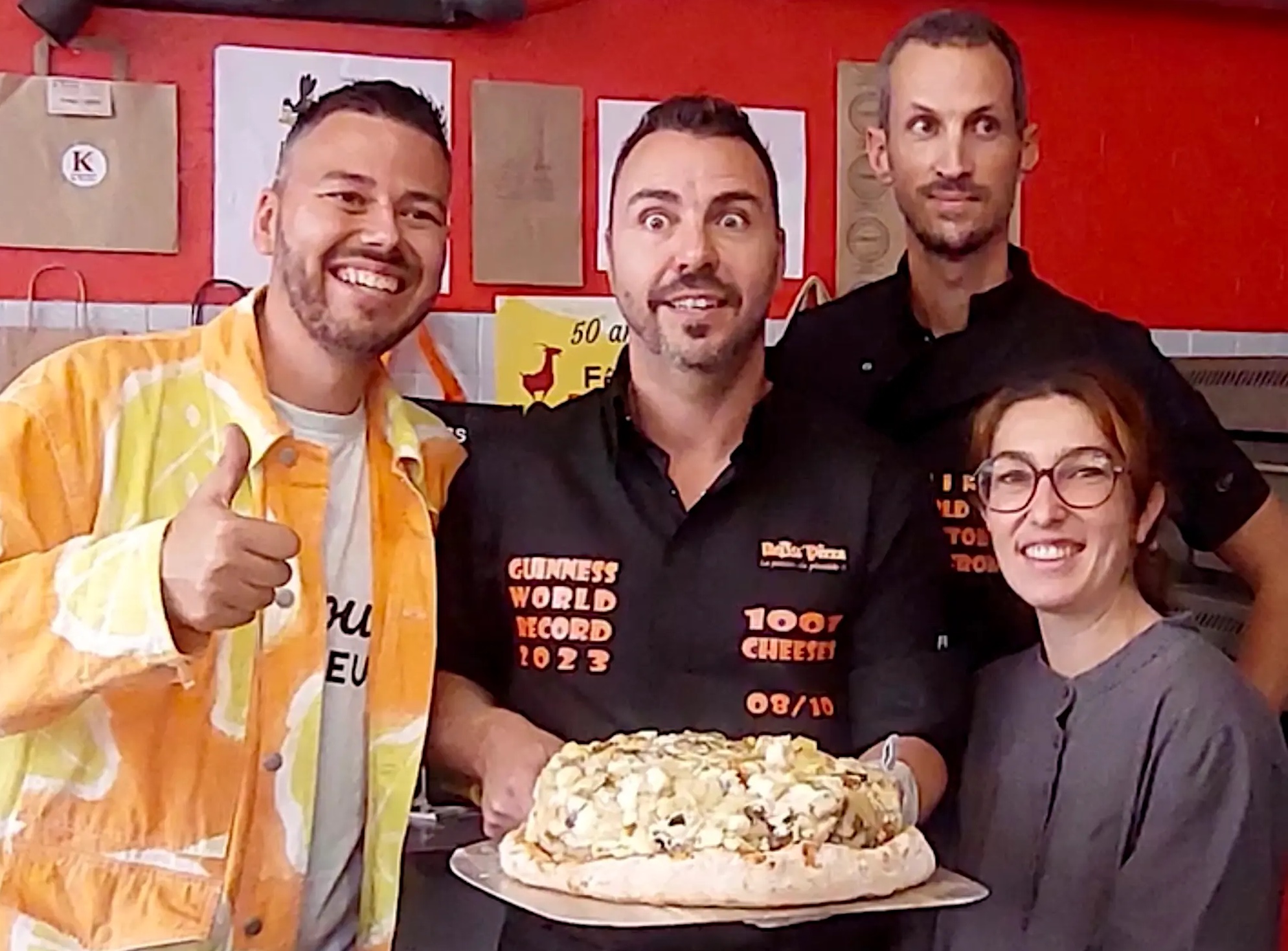This photo shows three men and one woman displaying a pizza topped with 1,001 different cheeses.