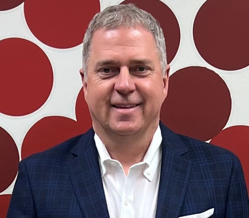 This photo shows Kevin King, with short graying hair, smiling and wearing a white dress shirt with a blue plaid sports coat.