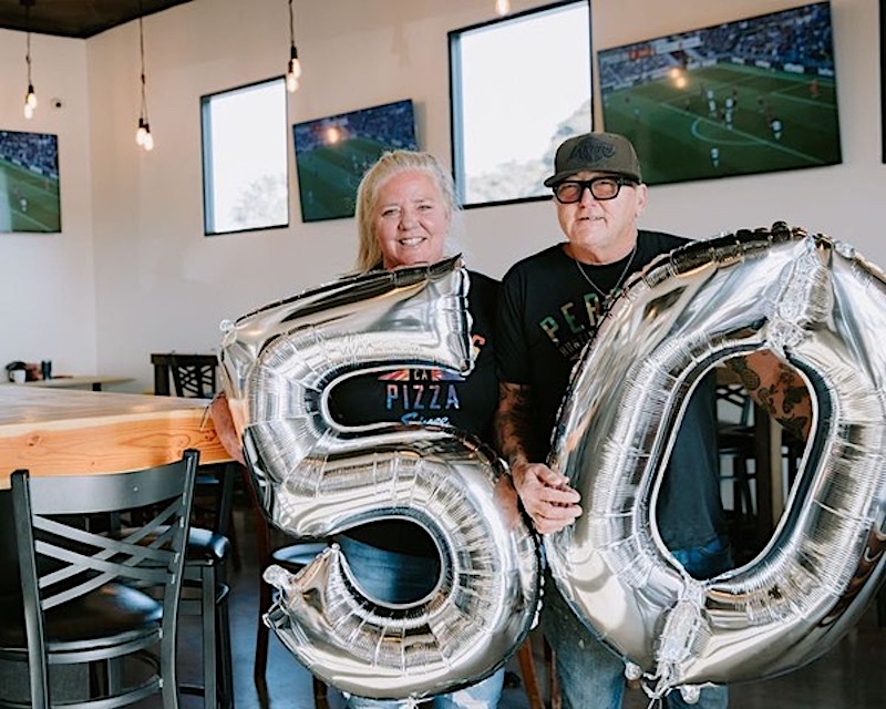 This photo shows the owners of Perry's. One is holding a balloon in the shape of the number 5, the other holding a balloon in the shape of the number 0.
