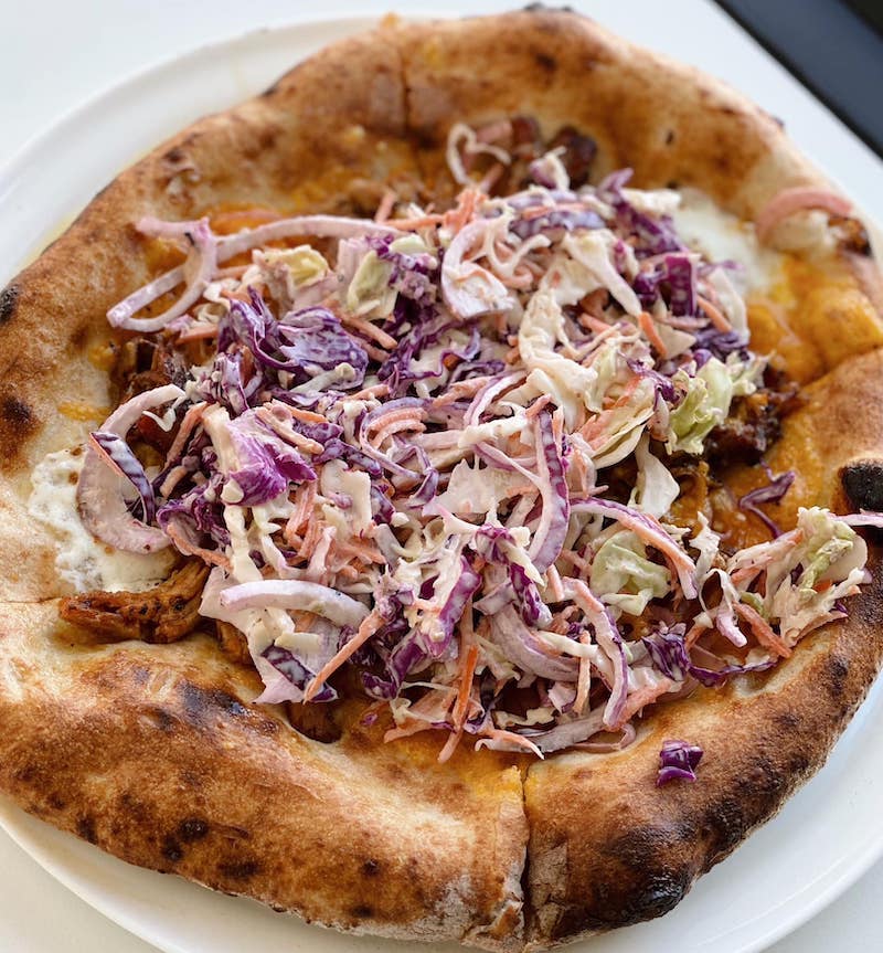 This photo shows a pizza topped with pulled pork and coleslaw