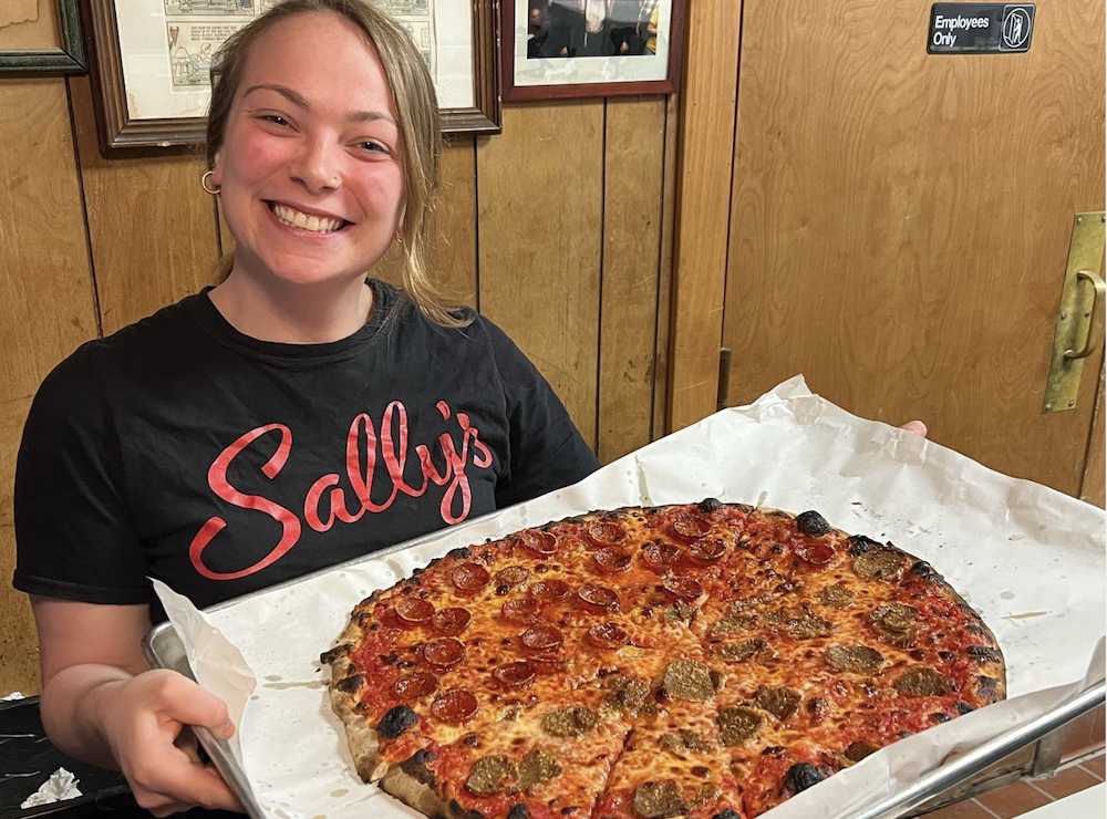 A woman at Sally's Apizza in New Haven holds up a New Haven-style pie.