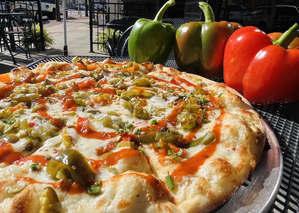 This photo shows a pizza flanked with red and green bell peppers.