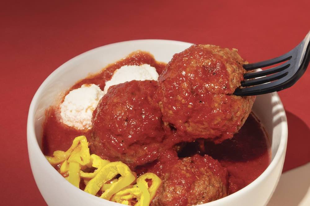 This photo shows a fork stuck in a big meatball, along with two other meatballs in the same bowl.