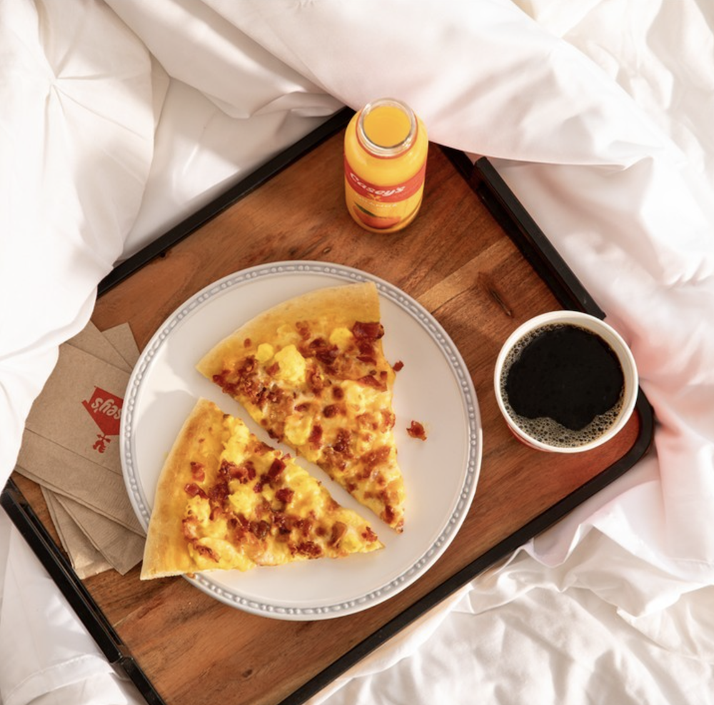 Two slices of breakfast pizza on a plate next to a Casey's orange juice and coffee. 