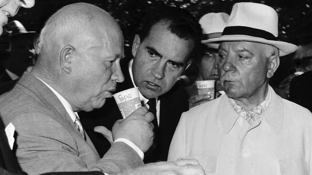 Nikita Khruschev sips Pepsi as Richard Nixon looks on.
