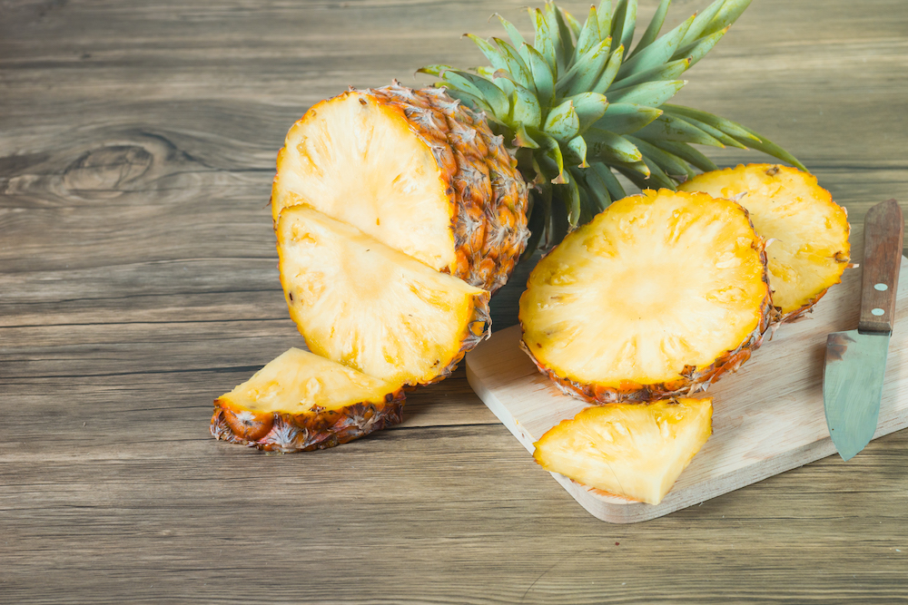 This photo shows a pineapple that has been cut into multiple slices against a wood-textured background.
