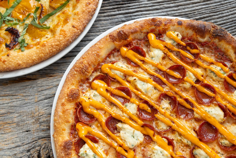 This photo shows the Spicy Calabrian pizza, with pepperoni, herbed ricotta, mozzarella and a red sauce. Next to it, there is a partial view of the Pizza Fumella.