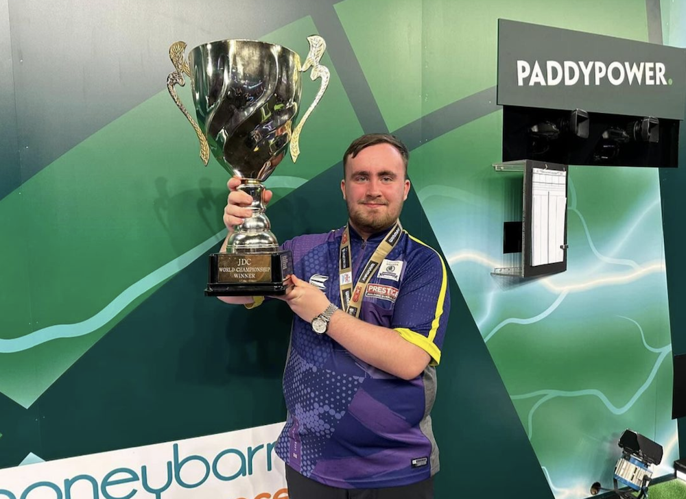 Luke Littler, a 16-year-old dart-throwing sensation from Warrington, England, holds up a trophy.