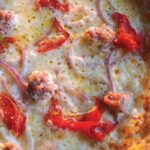 This photo shows a close-up of a pizza topped with red peppers, sausage and red onion.