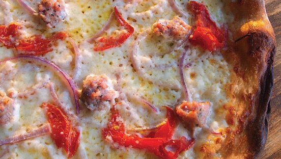 This photo shows a close-up of a pizza topped with red peppers, sausage and red onion.