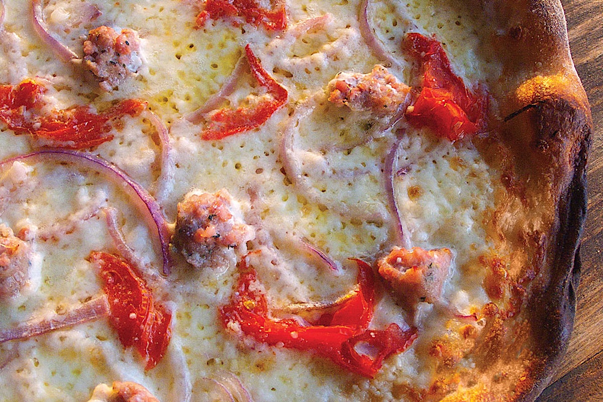 This photo shows a close-up of a pizza topped with red peppers, sausage and red onion.