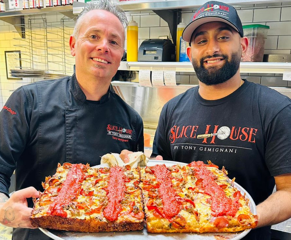 This photo shows Tony Gemignani and an unidentified man holding two square pizzas in the same round pan.