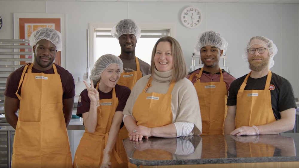 A group of six smiling people stand in a dough manufacturing facility.