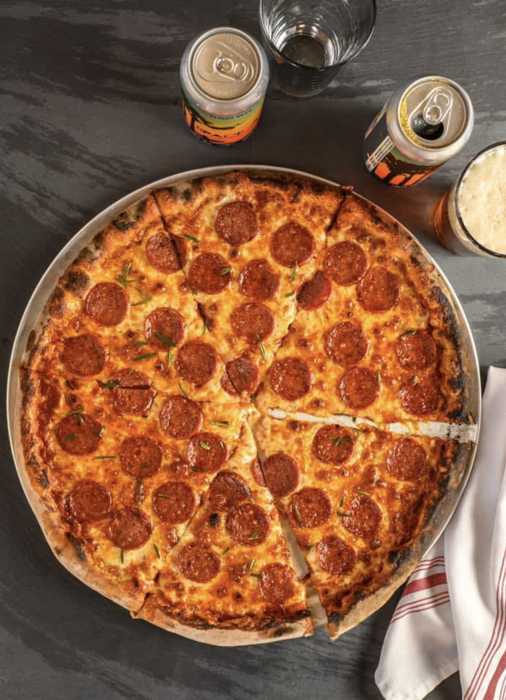 A pepperoni pizza sits with two beers.