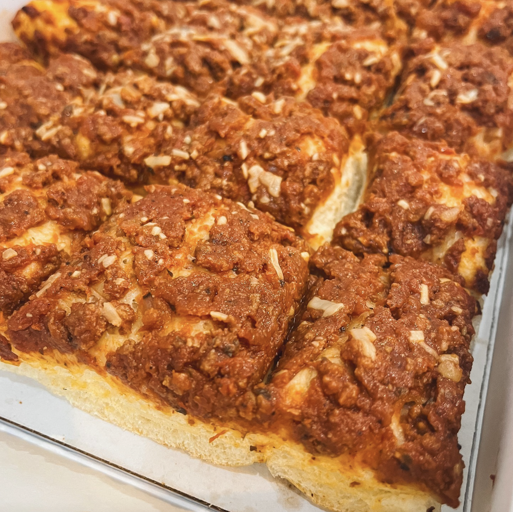 A shot of square pieces of room temperature pizza with sparing amounts of cheese.