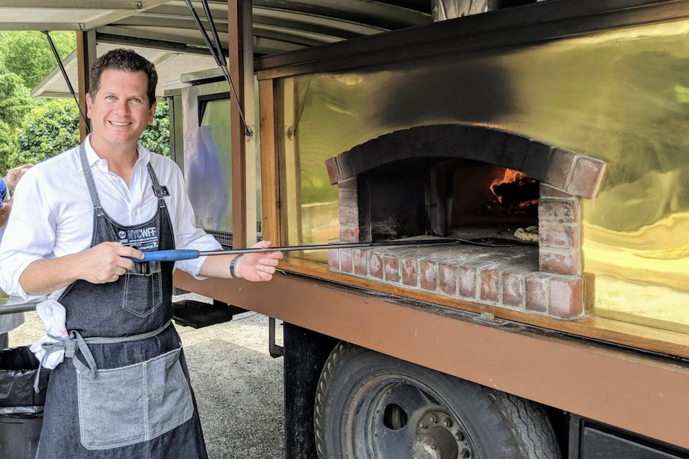 Dean Medico holds a pizza peel in a pizza oven on the back of a truck.