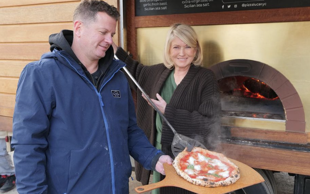Dean Medico holds a pizza peel as Martha Stewart holds one as well, with a pizza atop it.