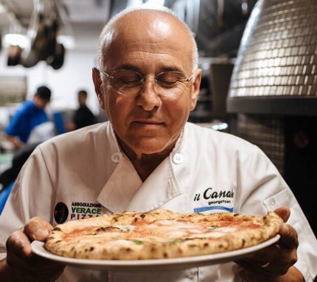 This photo shows Joe Faruggio holding a plated pizza to his chest and breathing in the delicious aroma.