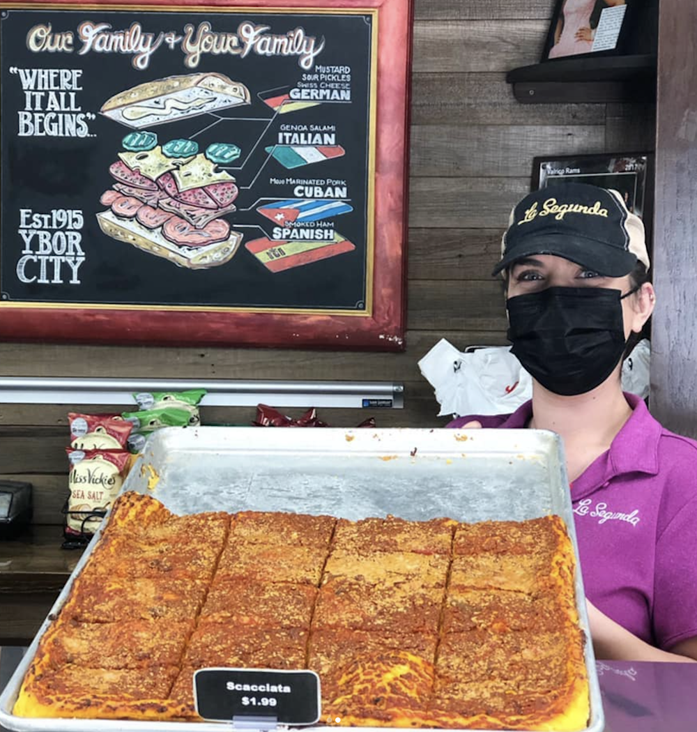 A woman holds up a tray of scachatta, a specialty bakery style of pizza in the Tampa, Florida area.