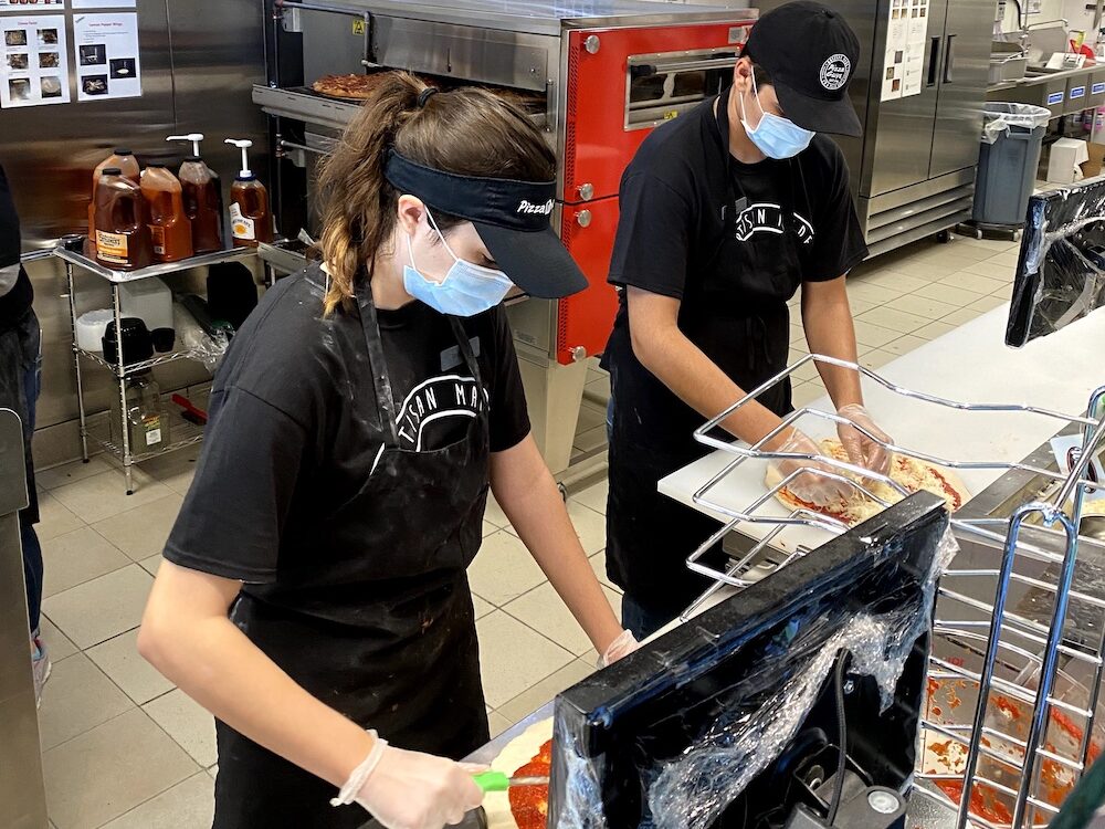 This photo shows two young pizza makers - a woman and a man - at work in the Pizza Guys kitchen.