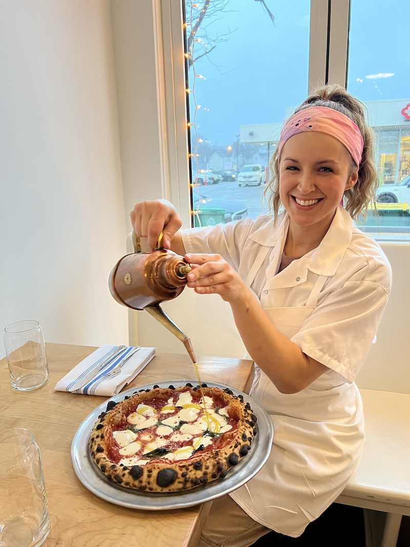 Amanda Jones smiles as she drizzles olive oil over a Margherita pizza.