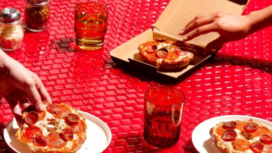 This photo, set against a red backdrop, shows three Pizza Hut bagels topped with pepperoni, two on a plate and one in a small box.