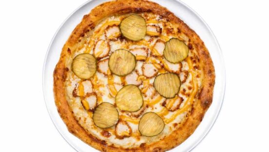 This photo shows a pizza topped with chicken nuggets and pickle slices