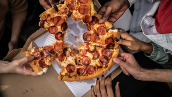 A group grabs slices from a communal pepperoni pizza.