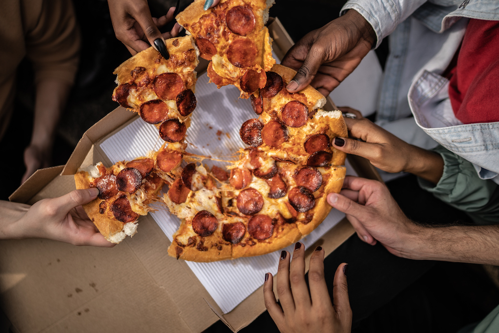 A group grabs slices from a communal pepperoni pizza.