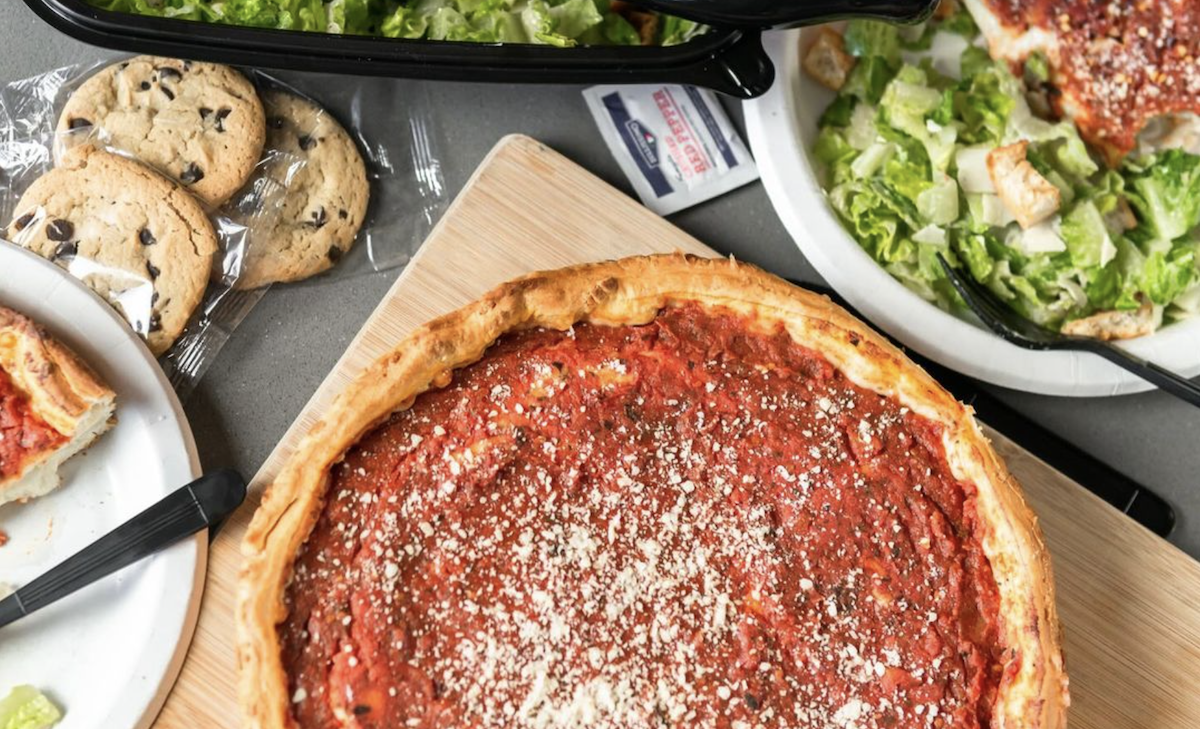 A Chicago deep-dish pizza sits on a cutting board surrounded by cookies, salads and other sides. The pizza is made by Giordano's, a pizza chain in Chicago.