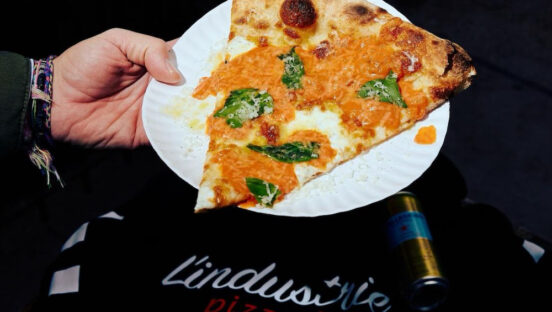 This photo shows a slice of a vodka pizza with fresh mozzarella set against a black L'Industrie t-shirt