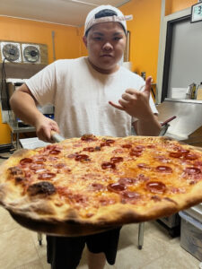 This photo shows Xavier holding a large pepperoni pizza 